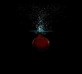 Photo of Pomegranate falling down into clear water against black background