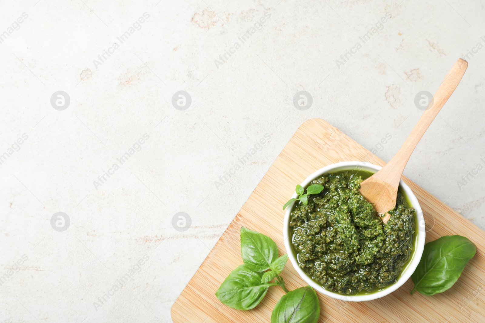 Photo of Board with homemade basil pesto sauce in bowl on table, top view. Space for text