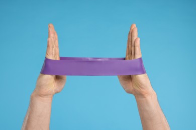 Photo of Man with elastic resistance band on light blue background, closeup of hands