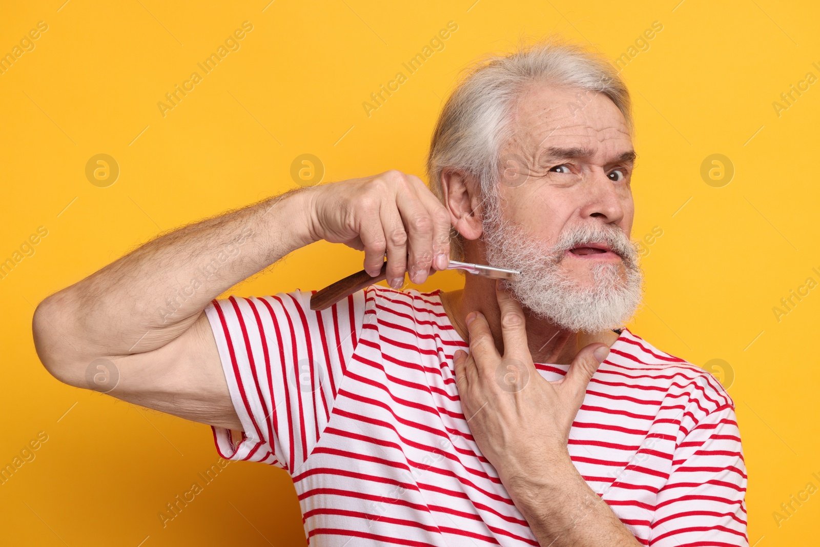 Photo of Senior man shaving beard with blade on orange background