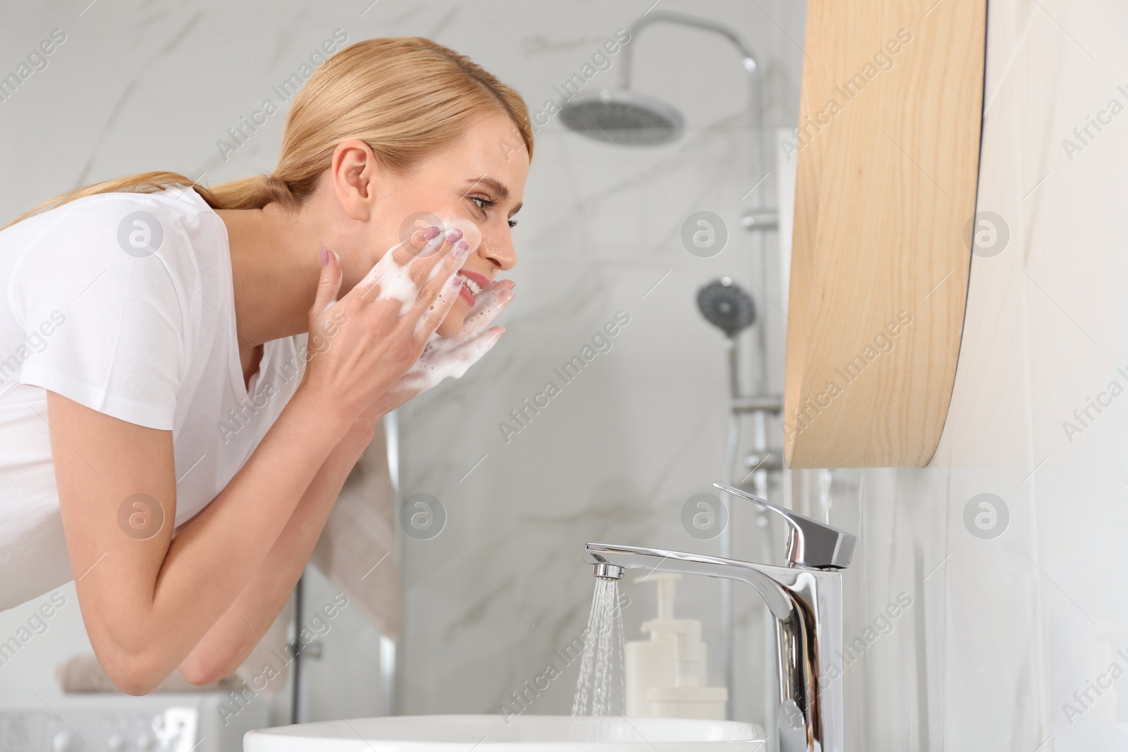 Photo of Happy young woman washing face in bathroom