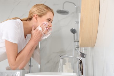 Happy young woman washing face in bathroom