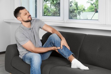 Photo of Man suffering from pain in leg on sofa at home