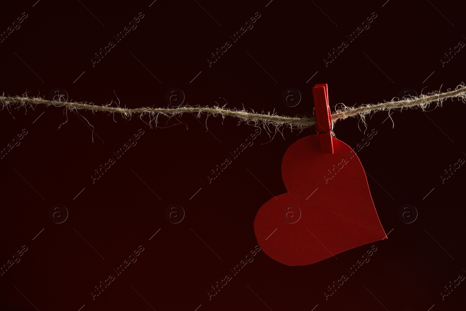 Photo of Red paper heart on rope against burgundy background, space for text. Broken heart