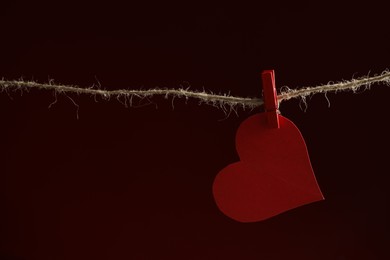 Photo of Red paper heart on rope against burgundy background, space for text. Broken heart