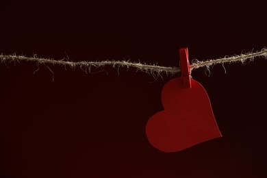 Red paper heart on rope against burgundy background, space for text. Broken heart