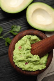 Mortar with delicious guacamole and ingredients on black wooden table, flat lay