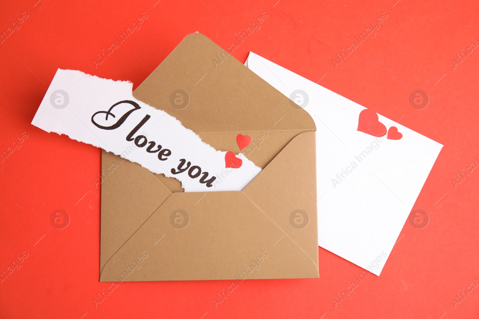 Photo of Sheet of paper with phrase I Love You and envelopes on red background, flat lay