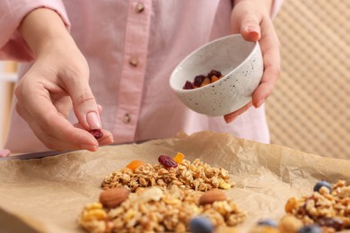 Photo of Making granola bars. Woman with dry fruits at table in kitchen, closeup