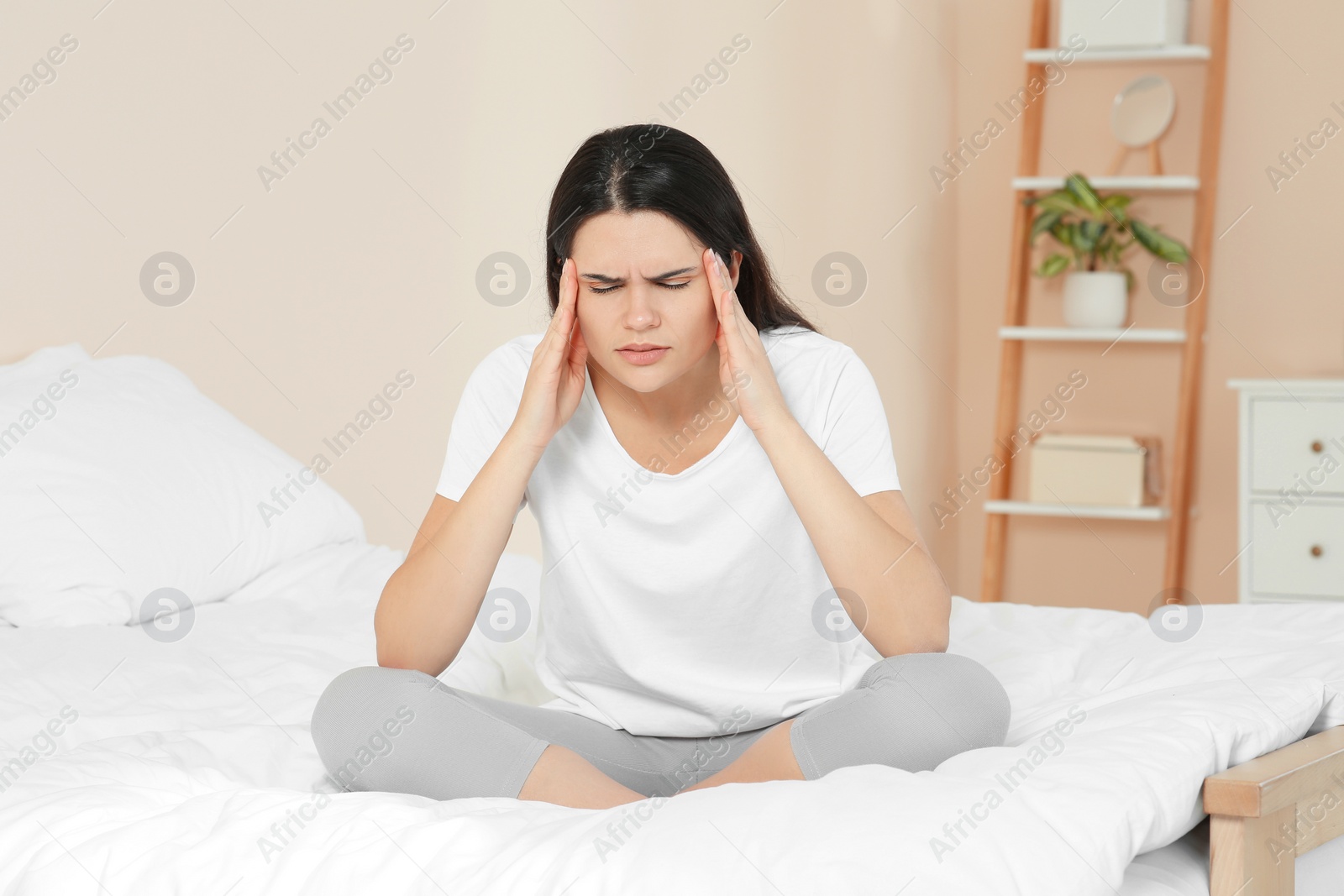 Photo of Young woman suffering from headache on bed at home. Hormonal disorders