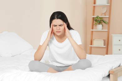 Young woman suffering from headache on bed at home. Hormonal disorders