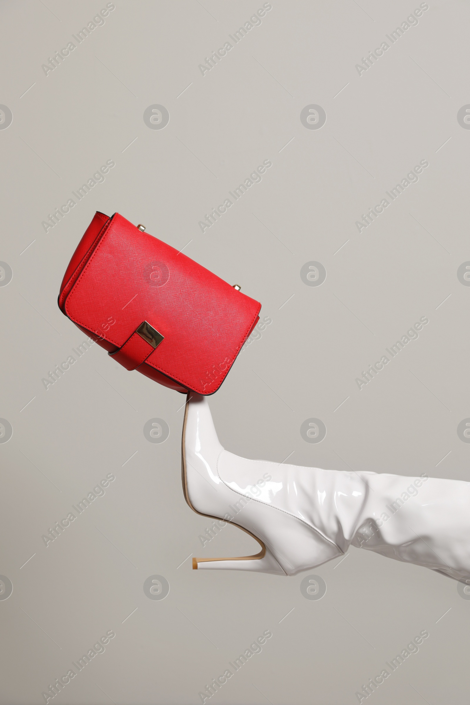 Photo of Woman wearing white long shoes with red leather bag on light background, closeup