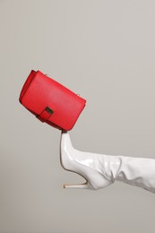 Photo of Woman wearing white long shoes with red leather bag on light background, closeup