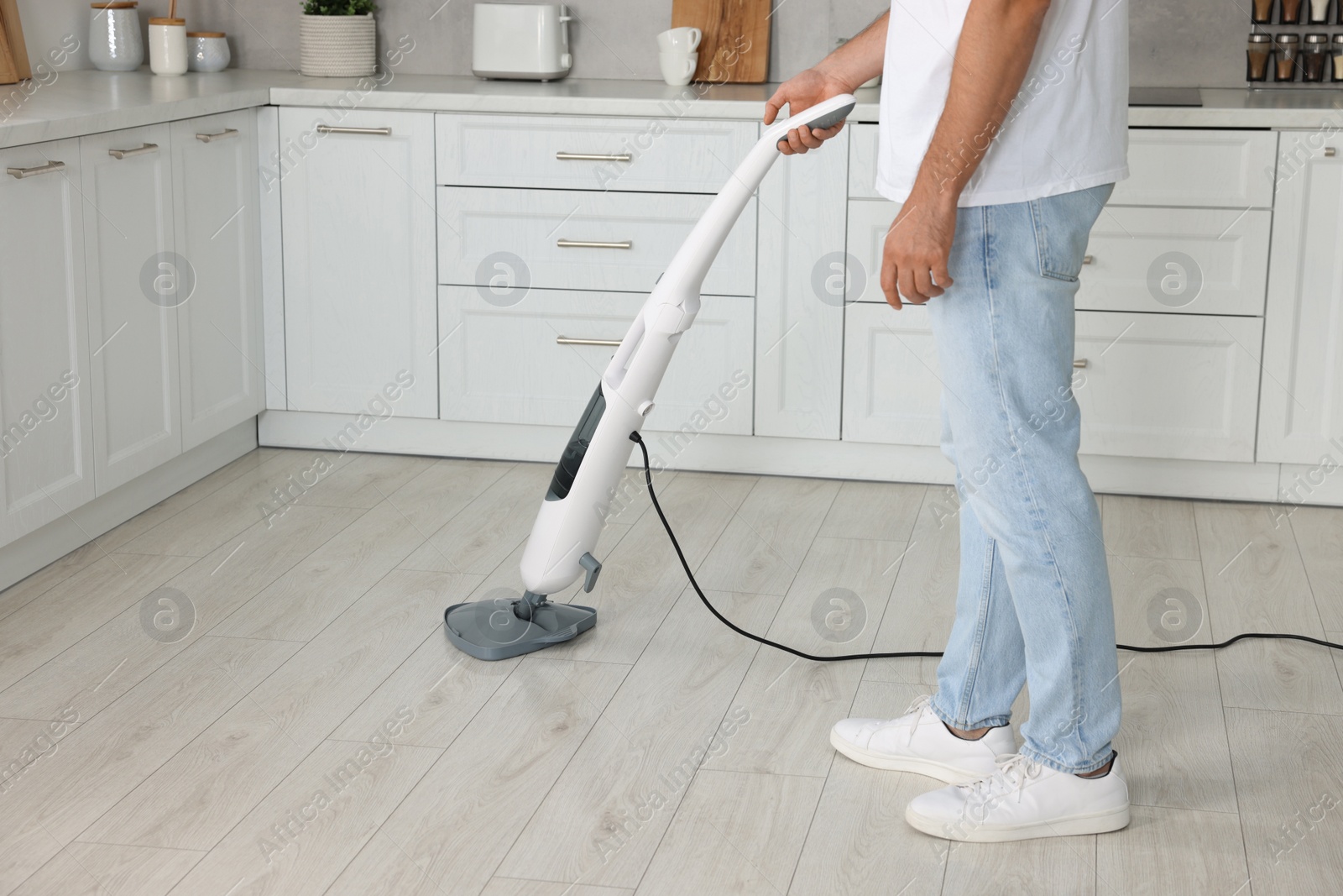 Photo of Man cleaning floor with steam mop in kitchen at home, closeup