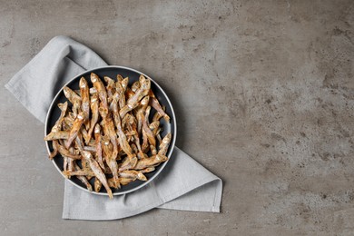 Photo of Plate of tasty dried anchovies and napkin on grey table, top view. Space for text