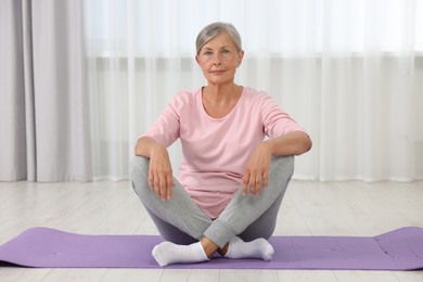 Photo of Senior woman sitting on mat at home. Yoga practice