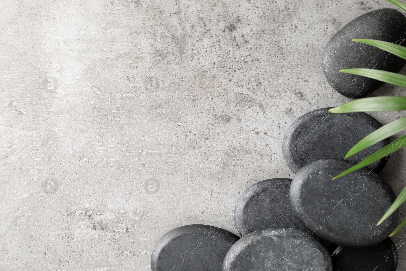 Photo of Spa stones and palm leaf on grey table, flat lay with space for text