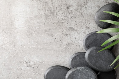 Spa stones and palm leaf on grey table, flat lay with space for text