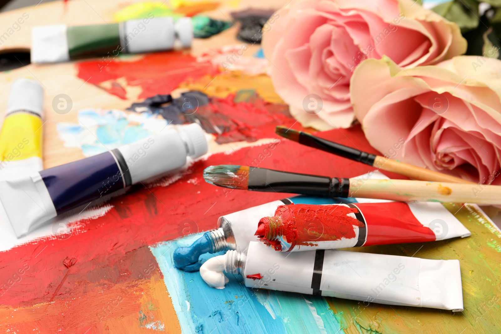 Photo of Tubes of colorful oil paints, flowers and brushes on canvas with abstract painting