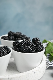 Photo of Tray with bowls of tasty blackberries on grey marble table against blue background