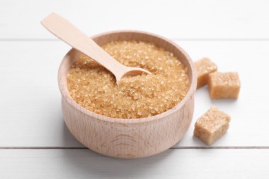 Photo of Brown sugar and spoon in bowl on white wooden table, closeup