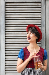 Young woman with cup of tasty lemonade near wooden wall