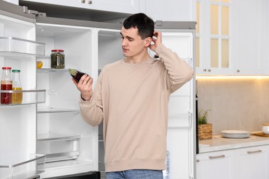 Upset man with eggplant near empty refrigerator in kitchen