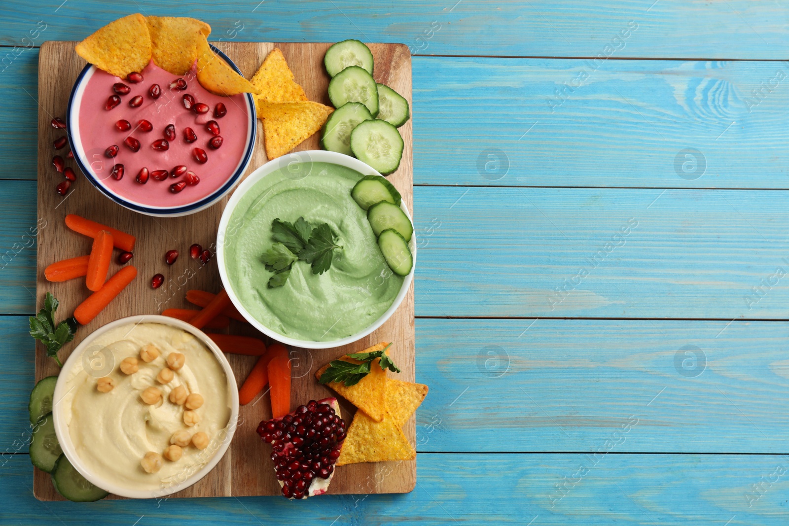 Photo of Composition with delicious hummuses on light blue wooden table, top view. Space for text