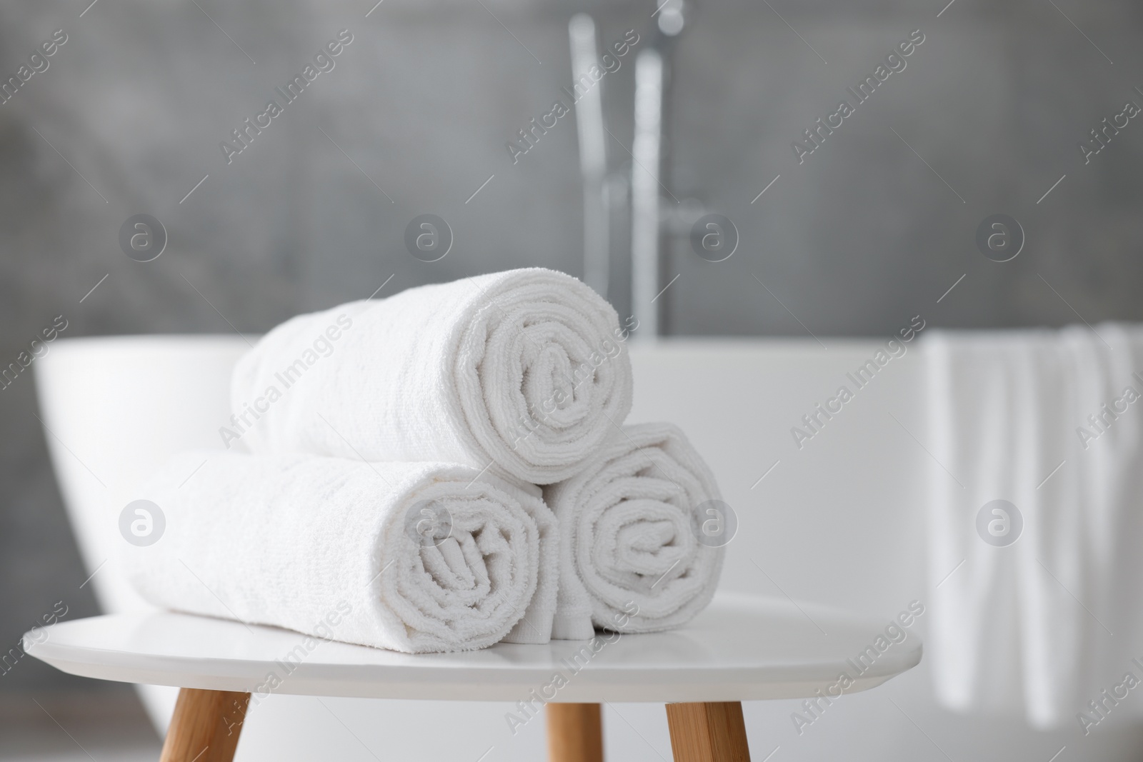 Photo of Rolled white towels on stool in bathroom. Space for text