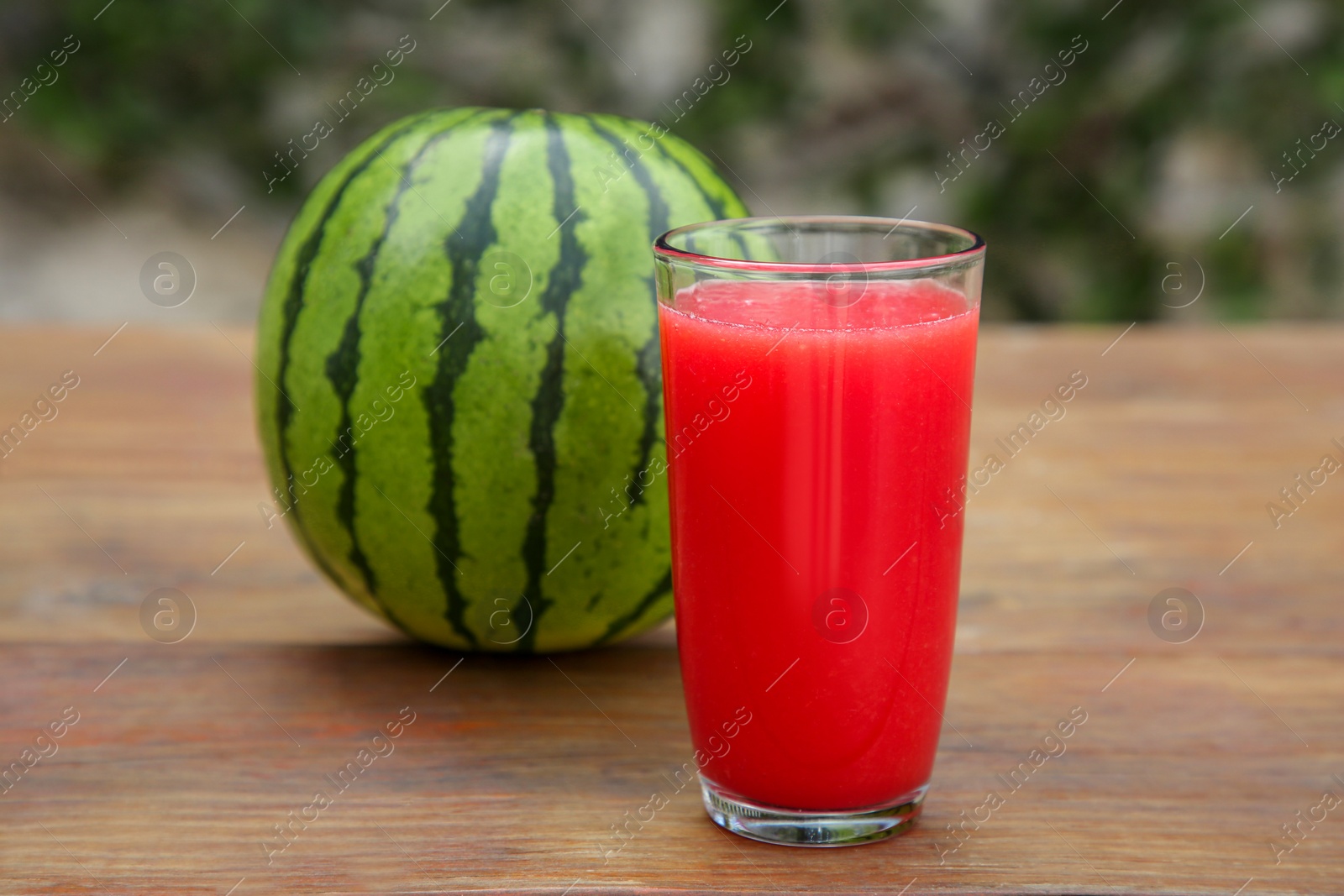 Photo of Delicious ripe watermelon and glass of fresh juice on wooden table outdoors