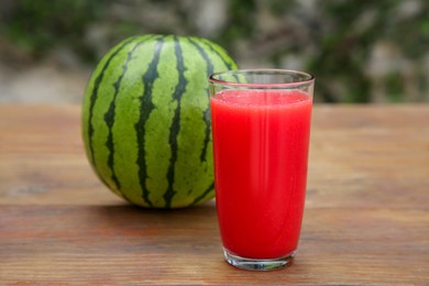 Photo of Delicious ripe watermelon and glass of fresh juice on wooden table outdoors