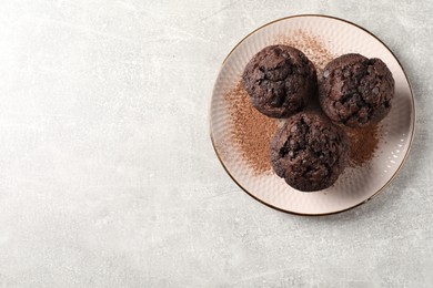 Photo of Delicious chocolate muffins and cacao powder on light grey table, top view. Space for text