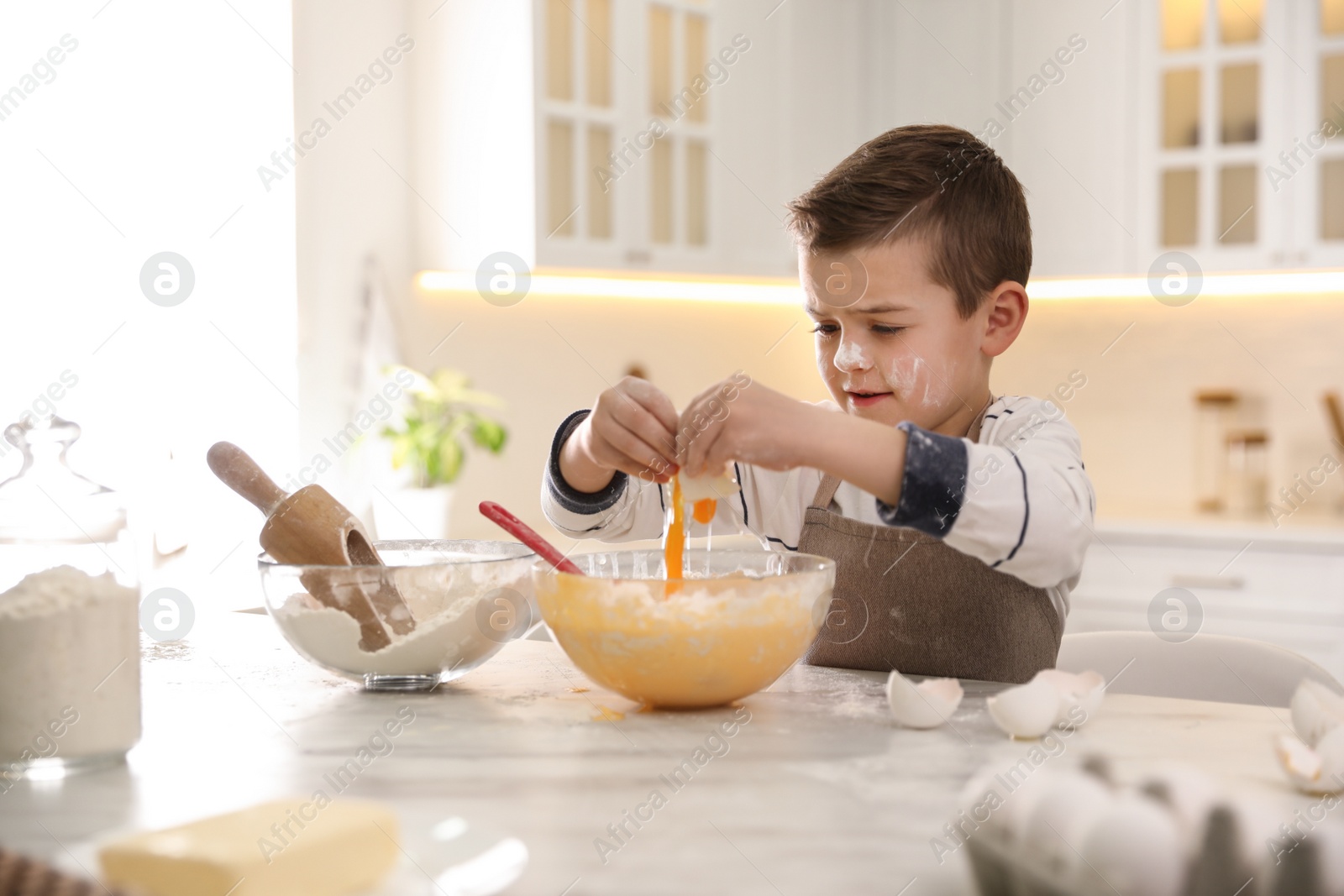 Photo of Cute little boy cooking dough at table in kitchen