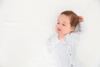 Photo of Adorable baby on white sheet, top view. Space for text