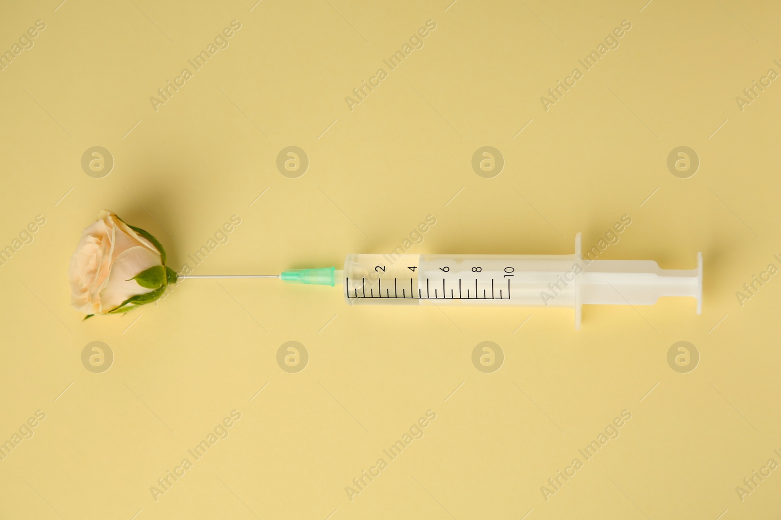 Photo of Medical syringe and beautiful rose on pale yellow background, top view