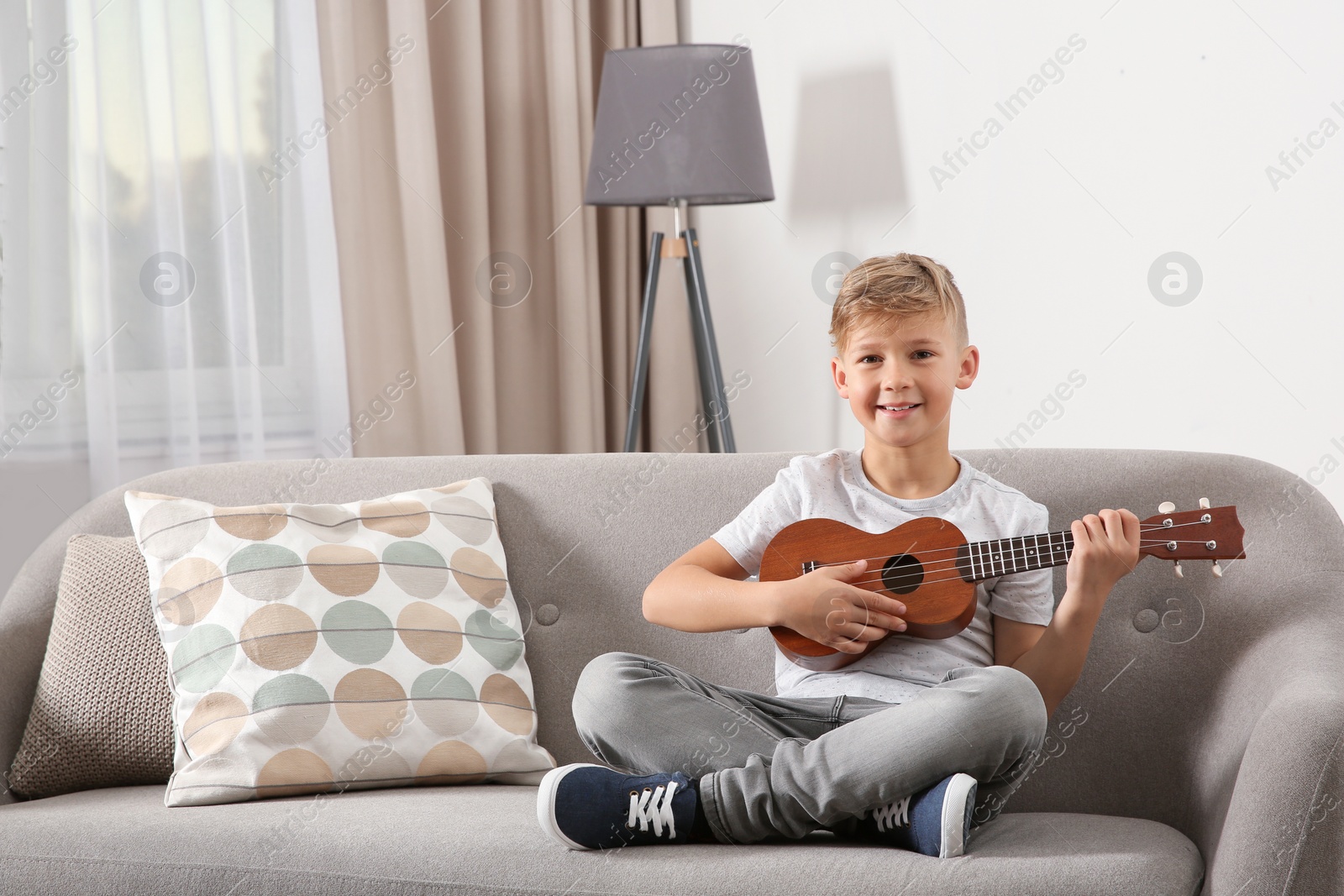 Photo of Little boy playing guitar on sofa in room. Space for text