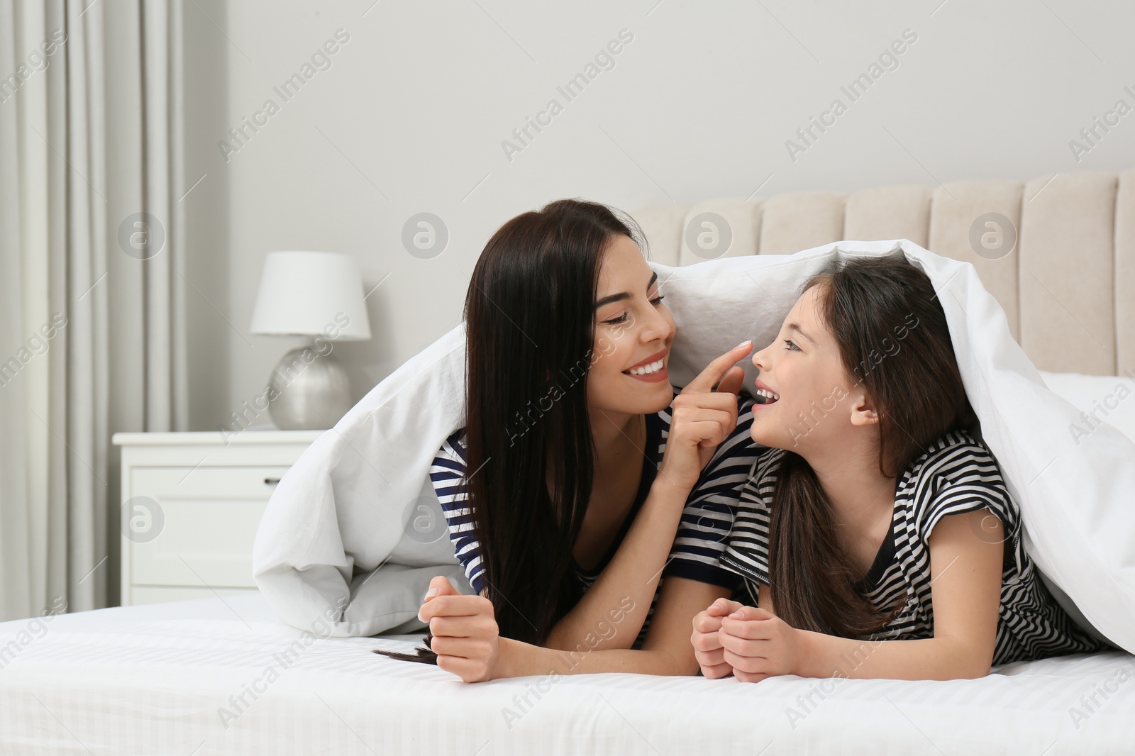 Photo of Young mother and her daughter under blanket in bed at home