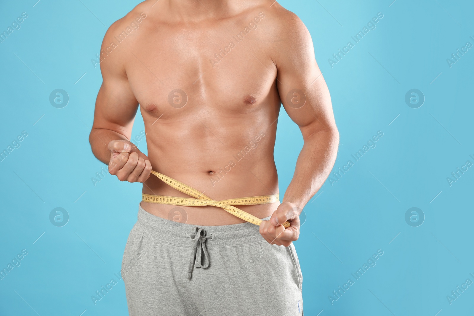 Photo of Young man with slim body using measuring tape on light blue background, closeup view