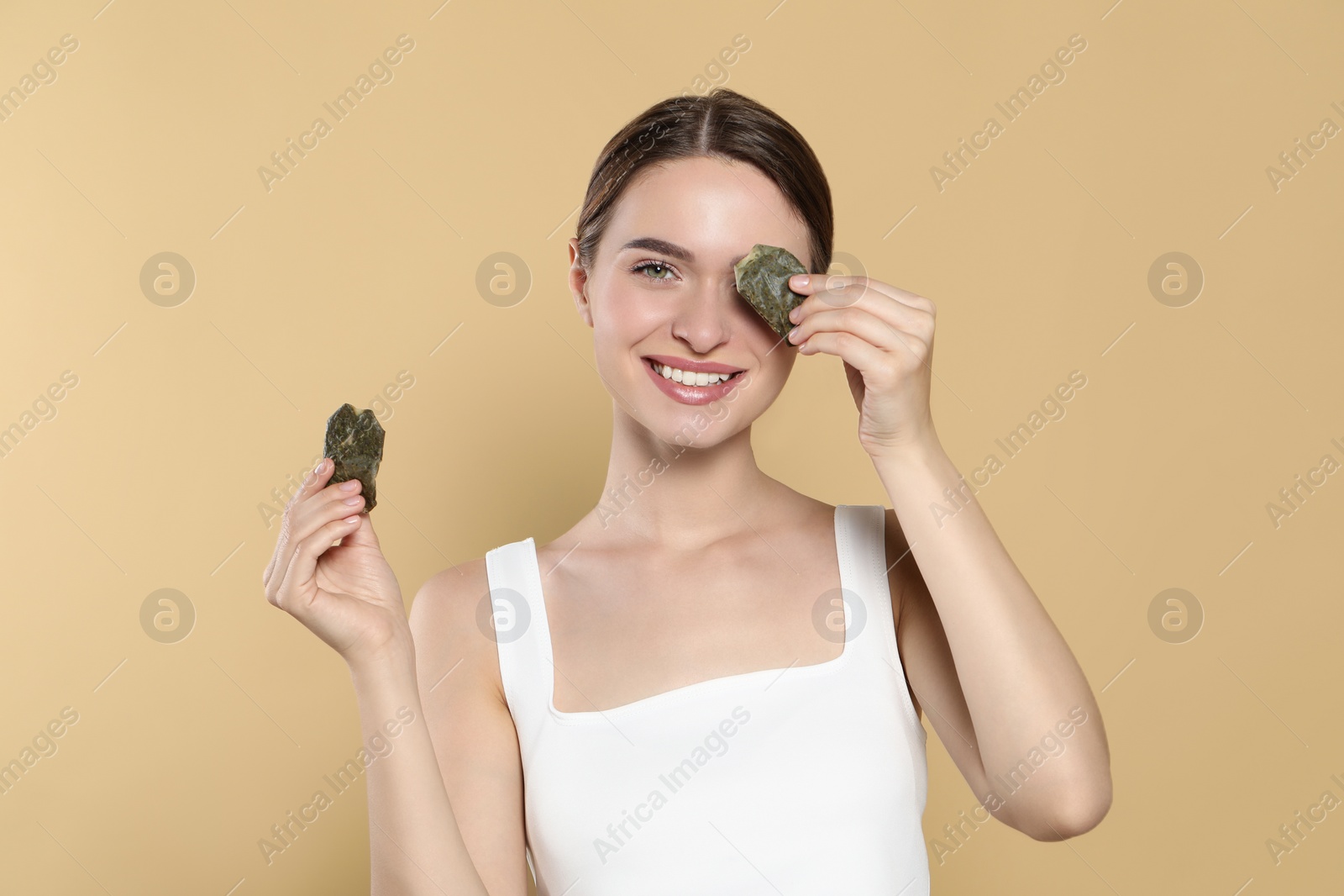 Photo of Young woman with green tea bags on beige background. Eye skin care