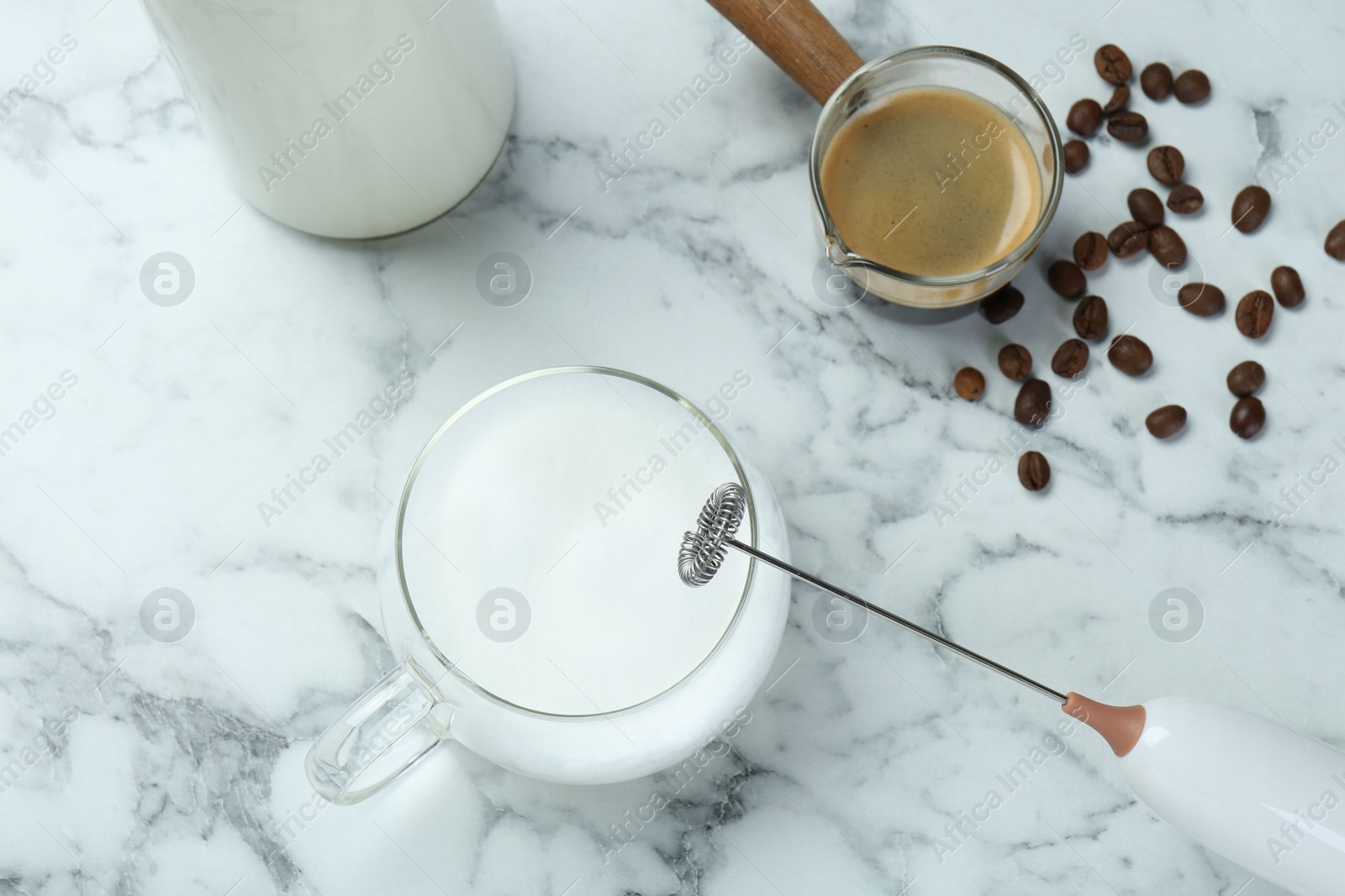 Photo of Mini mixer (milk frother), cup of milk and coffee on white marble table, flat lay