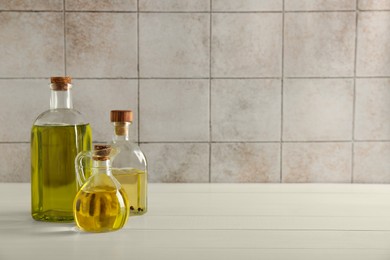 Photo of Vegetable fats. Different oils in glass bottles on white wooden table against tiled wall, space for text