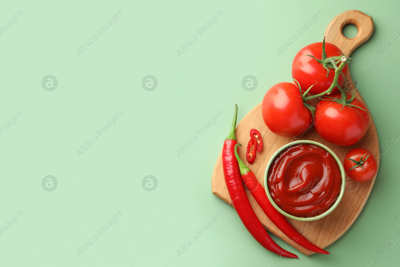 Photo of Bowl of tasty ketchup and ingredients on green table, top view. Space for text