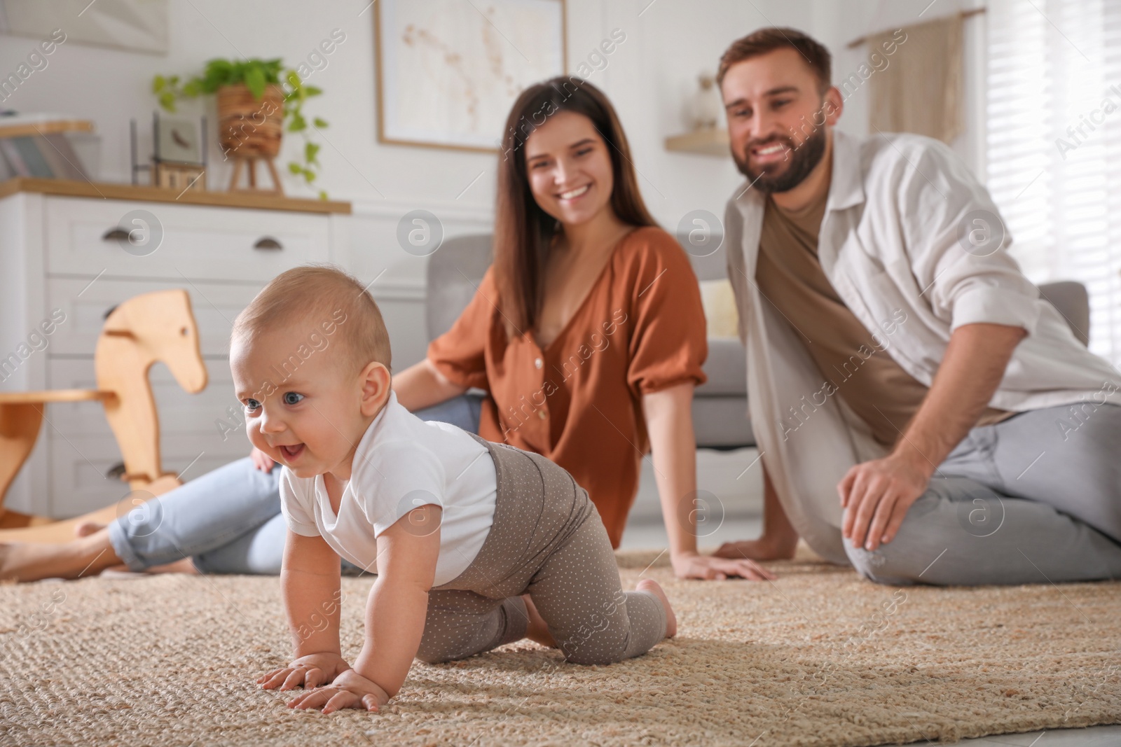 Photo of Happy parents watching their baby crawl on floor at home