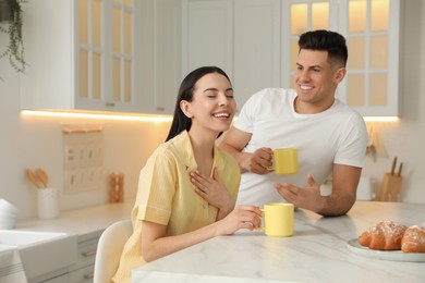 Happy couple wearing pyjamas during breakfast at table in kitchen