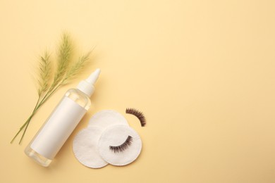 Photo of Bottle of makeup remover, cotton pads, false eyelashes and spikelets on yellow background, flat lay. Space for text