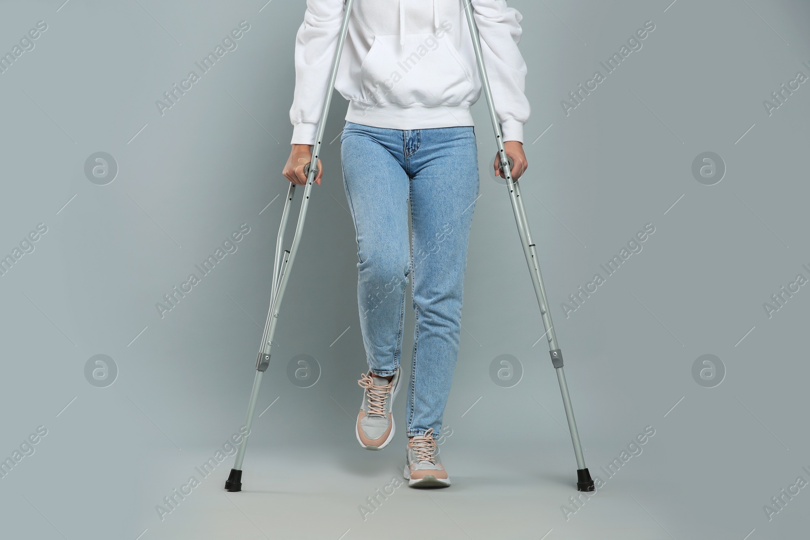 Photo of Young woman with axillary crutches on grey background, closeup