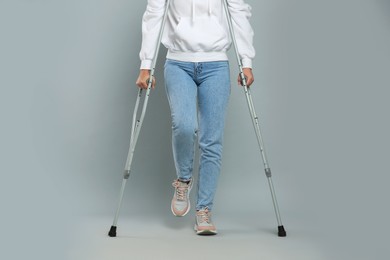 Photo of Young woman with axillary crutches on grey background, closeup