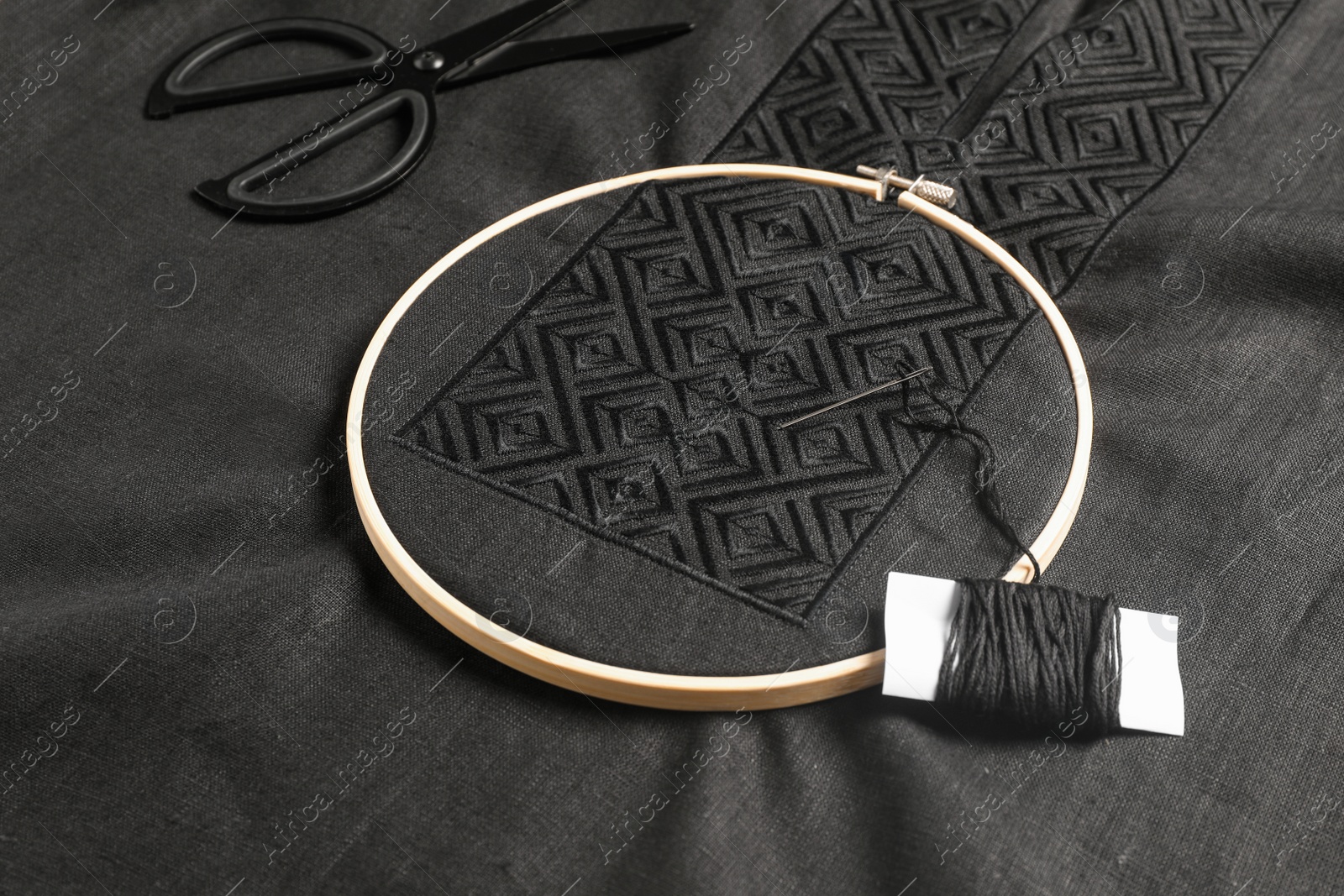 Photo of Embroidery hoop, thread and scissors on black shirt. Ukrainian national clothes