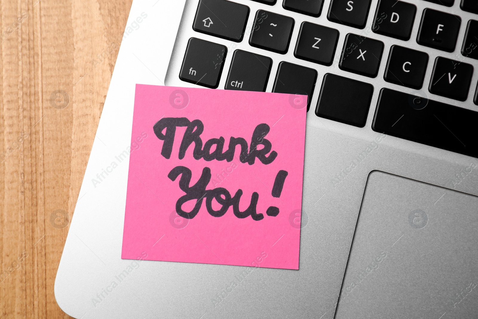 Photo of Pink paper note with phrase Thank You and laptop on wooden table, top view