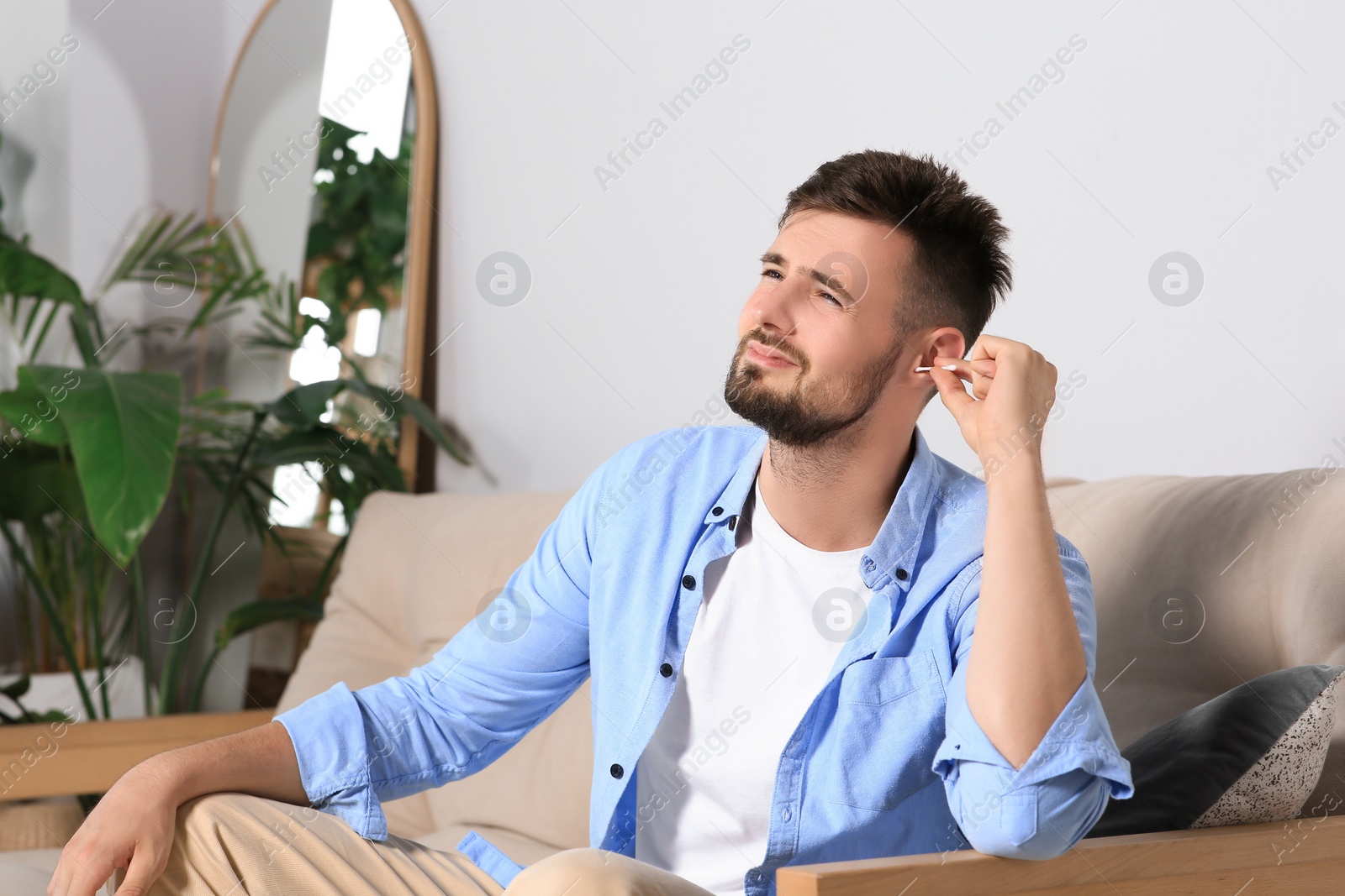 Photo of Young man cleaning ear with cotton swab at home